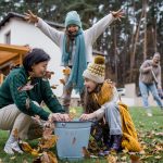 Szczęśliwe dziewczynki z babcią zbierają liście i wkładają je do wiaderka w ogrodzie jesienią